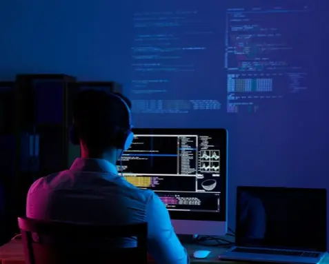 Developer working at a computer with code displayed on multiple screens, highlighting their problem-solving and analytical skills in identifying and resolving integration issues, and transforming complex business requirements into workable solutions.