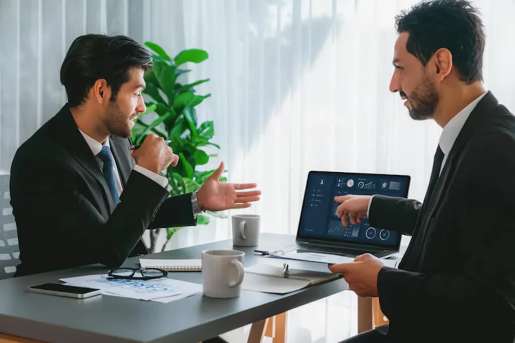 Two business professionals discussing AI product development strategies and performance metrics on a laptop to drive innovation and long-term growth