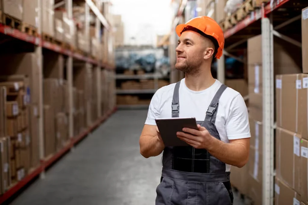 Warehouse worker holding a tablet in an aisle lined with packages, representing a logistics case study where AI-powered security solutions protected route optimization systems from malicious data interference—improving accuracy and delivery performance.