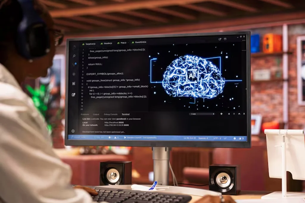 AI engineer working on a desktop with code and a glowing digital brain graphic labeled “AI,” representing AI outsourcing services focused on machine learning and deep learning model development for automation and data-driven decision-making.